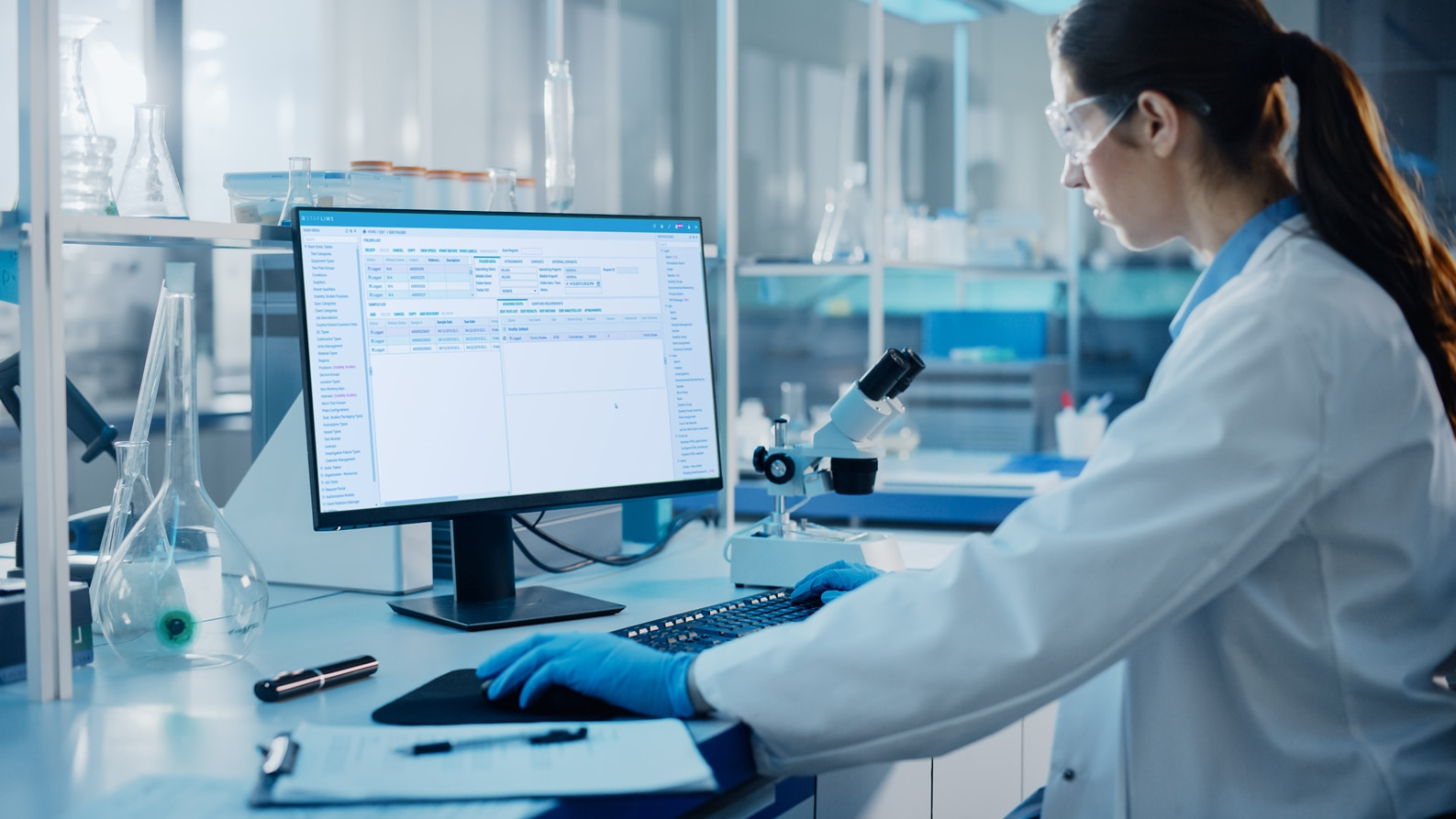 A woman laboratory manager works on a computer with protective gloves, reviewing STARLIMS laboratory information management system (LIMS) for Public Health